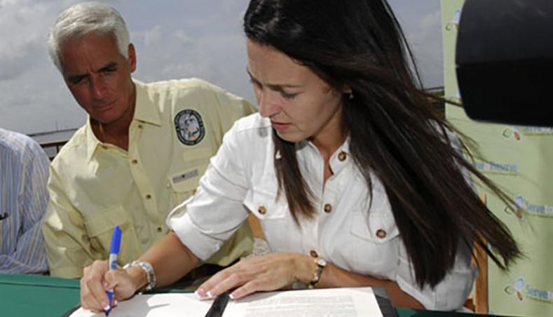 Gov. Charlie Crist stands as official witness as Shannon Estenoz, SFWMD vice chair, signs the U.S. Sugar deal's "Statement of Principles."